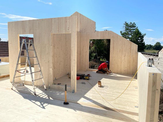 Wände aus Massivholzplatten während der Montage, ein Monteur arbeitet am Boden
